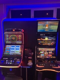 Zwei Gaming-Automaten mit bunten Displays in dunkel beleuchteter Gaming-Kabine